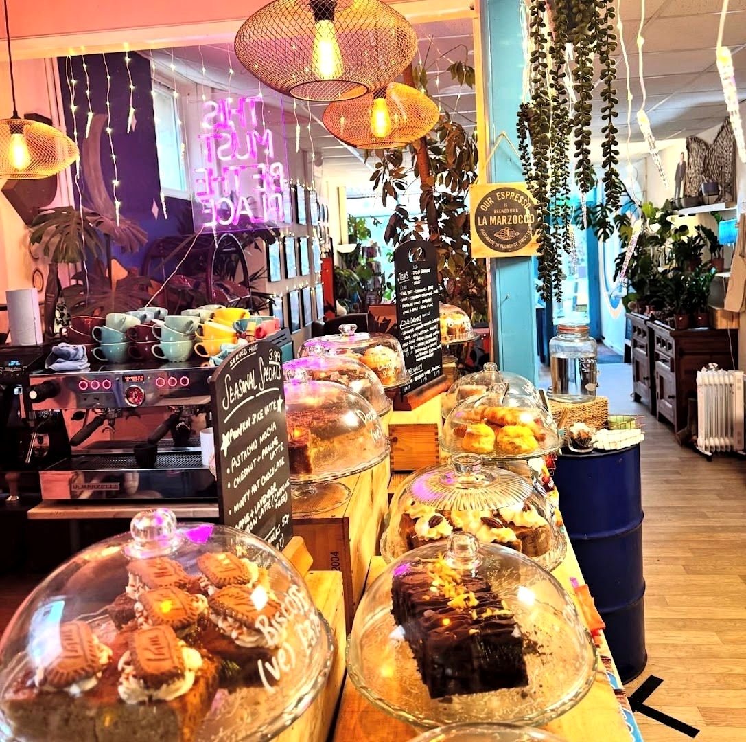 Inside Cactus Moon: cakes under glass domes on the counter, hanging plants, pendant lamps and a pink neon sign